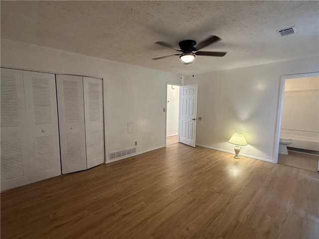 unfurnished bedroom with a closet, a textured ceiling, wood-type flooring, ceiling fan, and ensuite bathroom