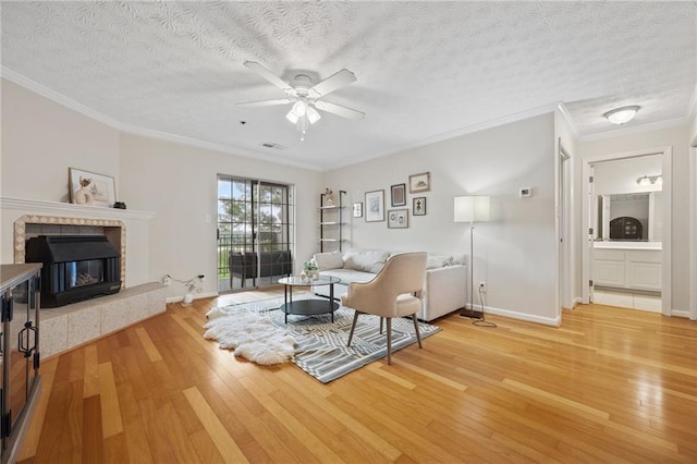 living room featuring a fireplace, crown molding, a ceiling fan, and light wood-type flooring