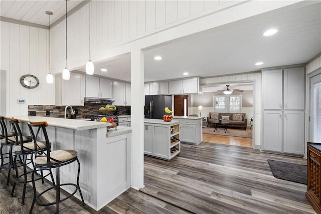 kitchen featuring dark wood-style flooring, light countertops, black fridge with ice dispenser, a peninsula, and under cabinet range hood