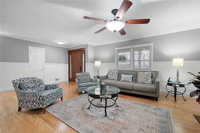 living area with ornamental molding, wainscoting, wood finished floors, and a ceiling fan