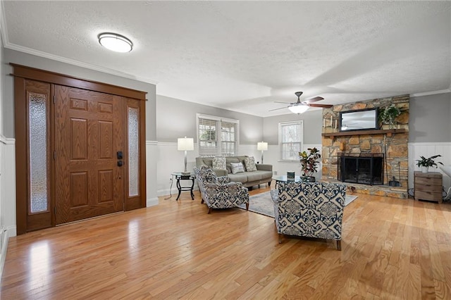 living area featuring ornamental molding, light wood-type flooring, a fireplace, and a textured ceiling