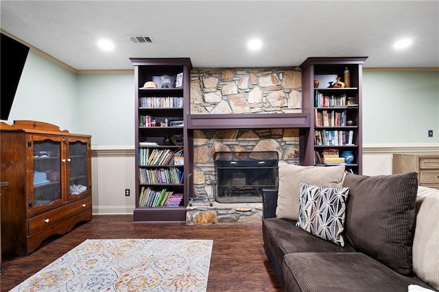 living area with crown molding, visible vents, wood finished floors, and a stone fireplace