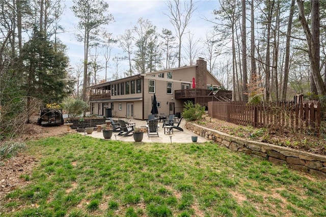 rear view of property featuring fence, a yard, a wooden deck, a chimney, and a patio area