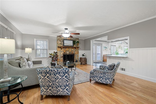 living room with a wainscoted wall, a fireplace, visible vents, light wood-style flooring, and a textured ceiling