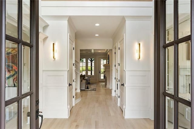 corridor featuring french doors, ornamental molding, and light hardwood / wood-style floors