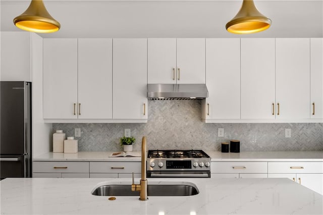 kitchen featuring light stone counters, freestanding refrigerator, white cabinets, stainless steel gas stove, and wall chimney range hood