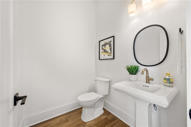 half bath with a sink, wood finished floors, toilet, and baseboards