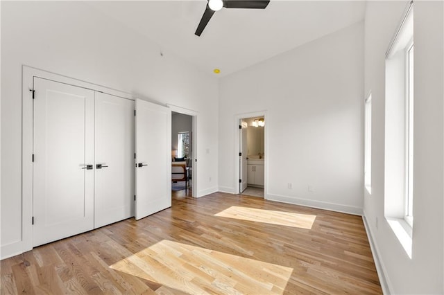 unfurnished bedroom with ensuite bathroom, a high ceiling, a ceiling fan, baseboards, and light wood-style floors