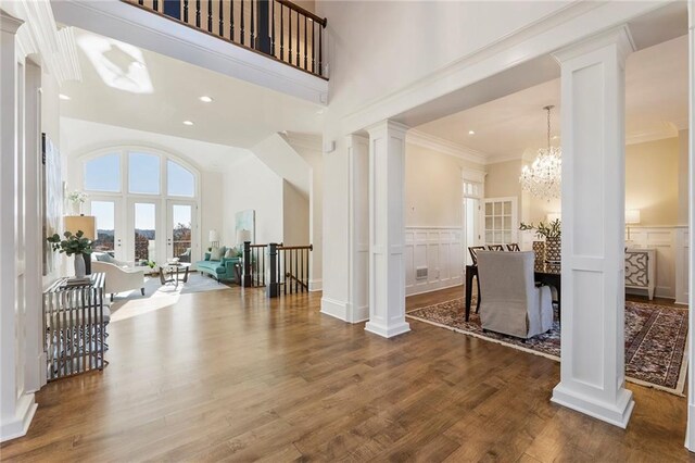 dining space with wood finished floors, ornate columns, crown molding, a decorative wall, and a chandelier