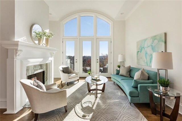 living room featuring wood finished floors, a high end fireplace, french doors, a towering ceiling, and crown molding