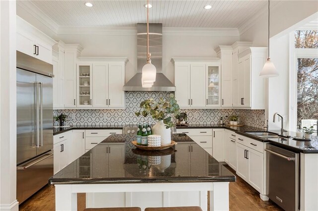 kitchen featuring dark countertops, wall chimney exhaust hood, crown molding, and a sink