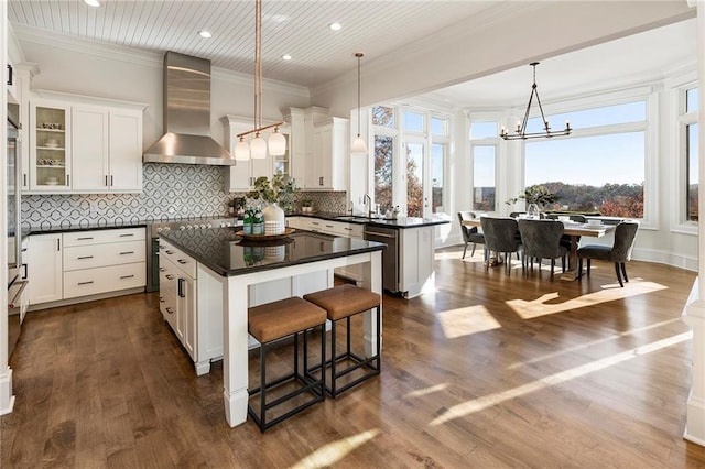 kitchen with dark countertops, a center island, ornamental molding, wall chimney exhaust hood, and a sink