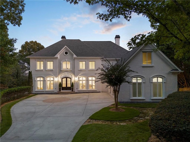 view of front of home featuring french doors, brick siding, driveway, and a chimney