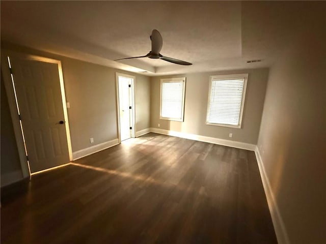 unfurnished bedroom with visible vents, dark wood-style floors, baseboards, a raised ceiling, and ceiling fan