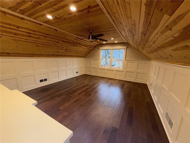 additional living space featuring visible vents, vaulted ceiling, wooden ceiling, a decorative wall, and dark wood-style flooring