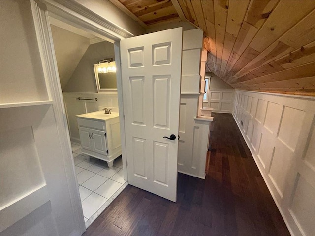 hallway featuring wood ceiling, lofted ceiling, dark wood-style flooring, a decorative wall, and a sink