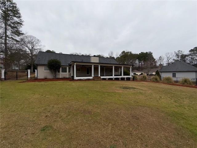 back of house with covered porch, a lawn, a chimney, and fence