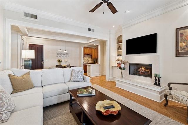 77 Peachtree Pl NE Unit 101, Atlanta, GA 30309 - living room featuring crown molding, ceiling fan, light wood-style floors, a fireplace, and built in shelves