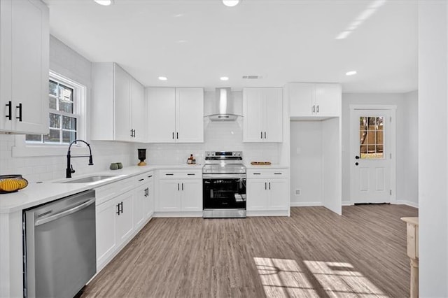 kitchen with wall chimney exhaust hood, light hardwood / wood-style floors, white cabinetry, appliances with stainless steel finishes, and sink