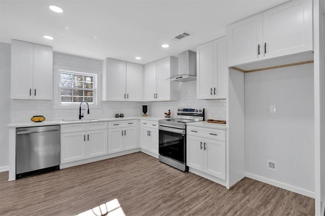 kitchen with stainless steel appliances, white cabinets, light hardwood / wood-style flooring, wall chimney range hood, and sink