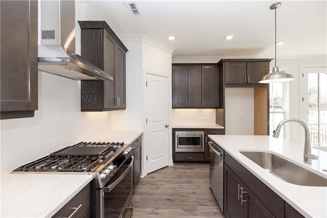 kitchen with visible vents, dark brown cabinets, wall chimney exhaust hood, a sink, and stainless steel appliances