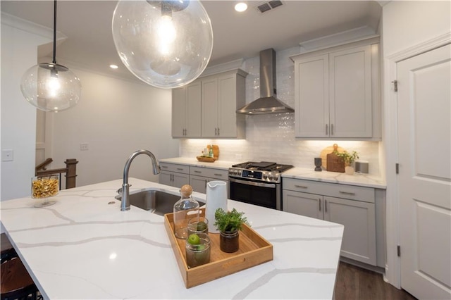 kitchen featuring gray cabinetry, a sink, visible vents, wall chimney exhaust hood, and gas range