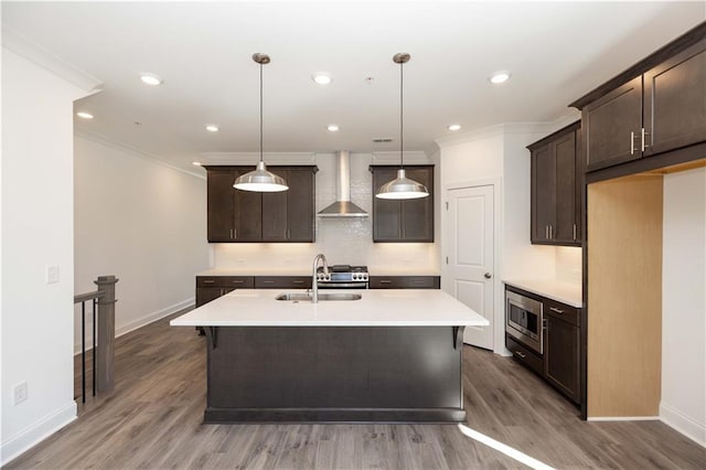 kitchen featuring dark brown cabinetry, a sink, wall chimney exhaust hood, baseboards, and ornamental molding