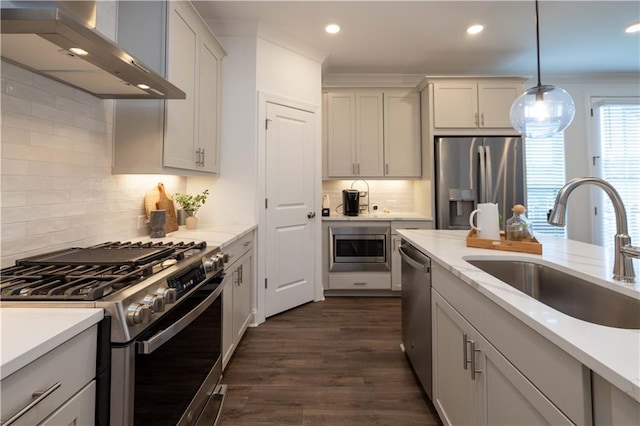 kitchen with dark wood-style floors, wall chimney exhaust hood, appliances with stainless steel finishes, pendant lighting, and a sink