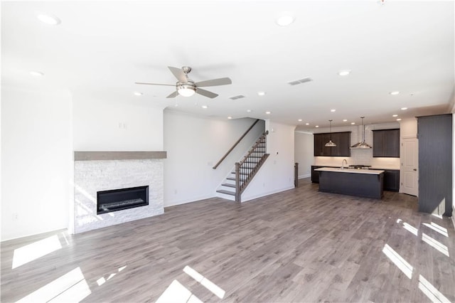 unfurnished living room with a ceiling fan, visible vents, a fireplace, light wood finished floors, and stairs