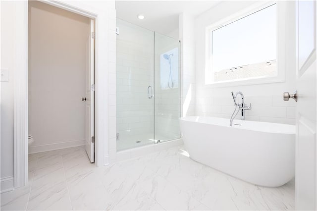 bathroom featuring toilet, marble finish floor, a freestanding tub, baseboards, and a stall shower