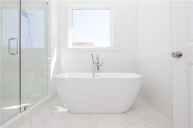 full bathroom featuring marble finish floor, a freestanding tub, tile walls, and a shower stall