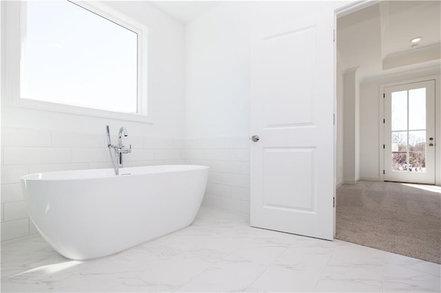 bathroom with tile walls, a soaking tub, marble finish floor, and a wealth of natural light