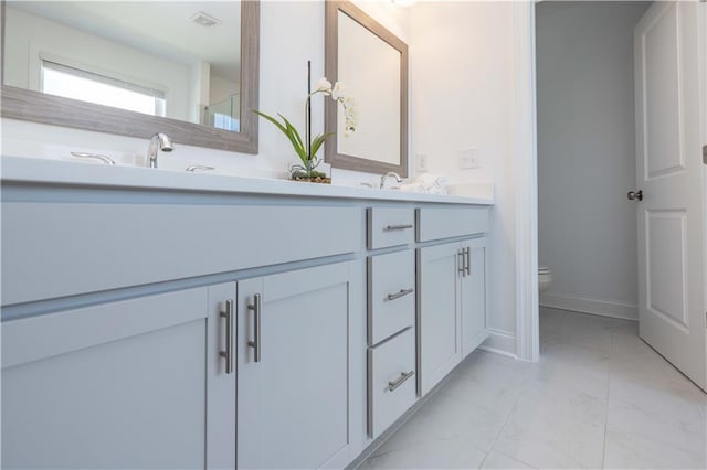 bathroom featuring toilet, visible vents, baseboards, marble finish floor, and double vanity