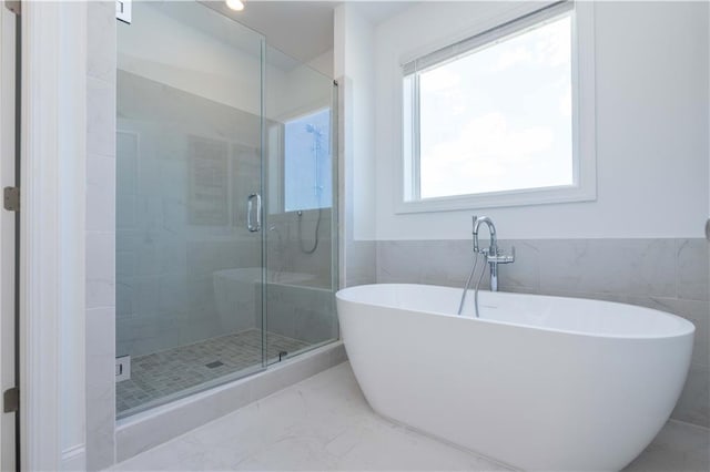 bathroom featuring a wainscoted wall, tile walls, a freestanding bath, marble finish floor, and a shower stall