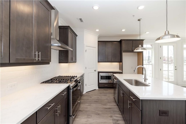 kitchen with visible vents, dark brown cabinets, wall chimney range hood, a sink, and stainless steel appliances