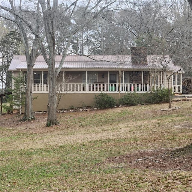 view of front of property featuring a porch, metal roof, a front yard, and a chimney