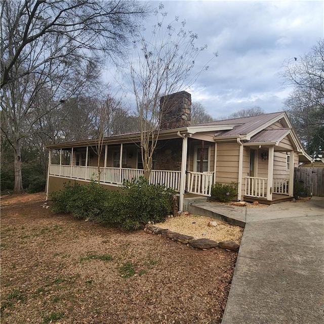 ranch-style home with metal roof, covered porch, and a chimney