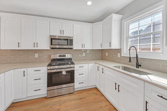 kitchen with light hardwood / wood-style floors, stainless steel appliances, sink, and white cabinets