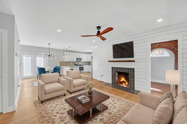 living room featuring light hardwood / wood-style flooring, a tiled fireplace, and ceiling fan with notable chandelier