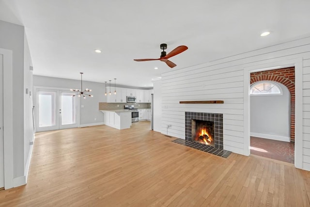 unfurnished living room featuring ceiling fan with notable chandelier, a fireplace, and light wood-type flooring