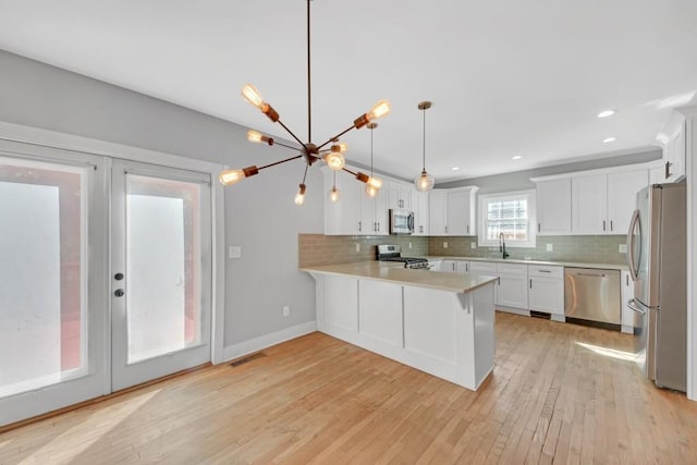 kitchen featuring kitchen peninsula, white cabinets, appliances with stainless steel finishes, light wood-type flooring, and pendant lighting