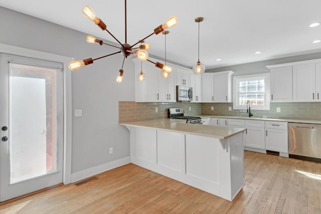 kitchen featuring kitchen peninsula, hanging light fixtures, appliances with stainless steel finishes, white cabinetry, and light hardwood / wood-style floors