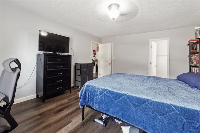 bedroom with a textured ceiling, dark wood-type flooring, and a spacious closet