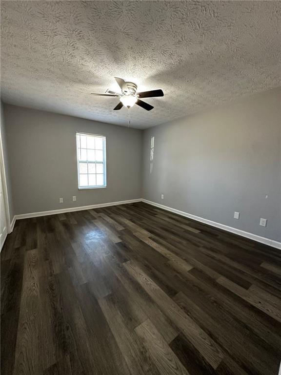 empty room with a textured ceiling, dark wood-type flooring, and ceiling fan