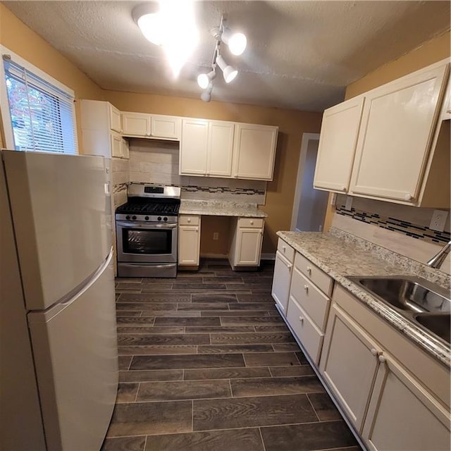 kitchen with wood finish floors, stainless steel gas stove, a sink, freestanding refrigerator, and decorative backsplash