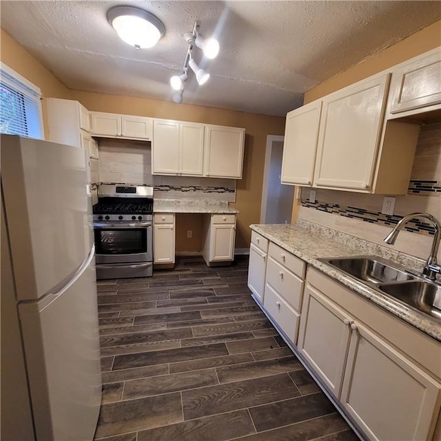 kitchen featuring stainless steel gas range oven, tasteful backsplash, wood finish floors, freestanding refrigerator, and a sink