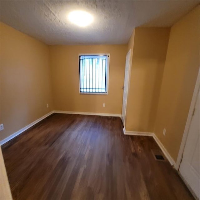 spare room with visible vents, baseboards, a textured ceiling, and dark wood finished floors