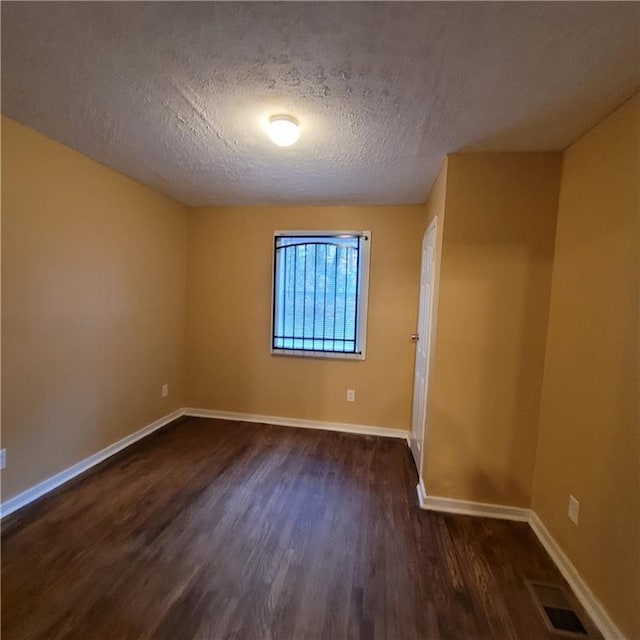 empty room with visible vents, baseboards, and dark wood finished floors