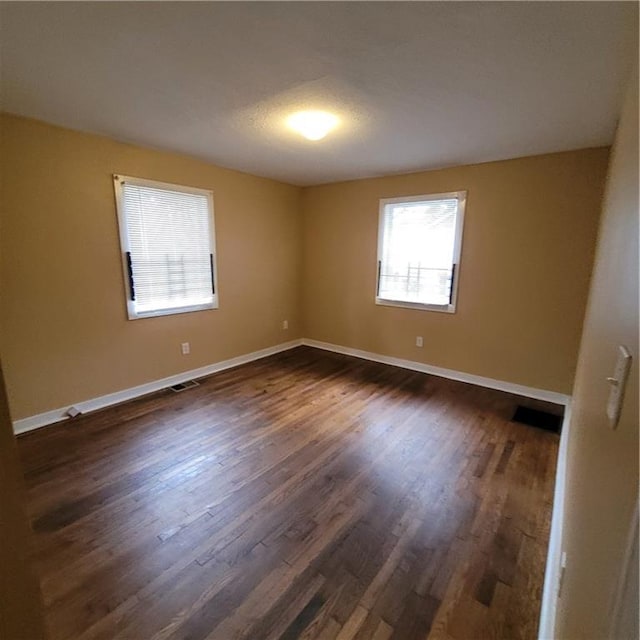 unfurnished room with dark wood-style floors, visible vents, and baseboards