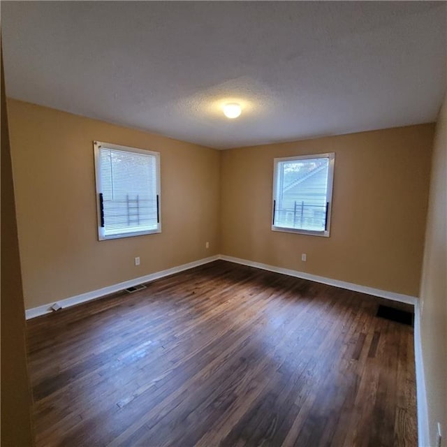 empty room with visible vents, a textured ceiling, baseboards, and dark wood-style flooring